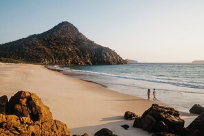 Une plage avec une grande formation rocheuse et une personne qui se promène le long du rivage.