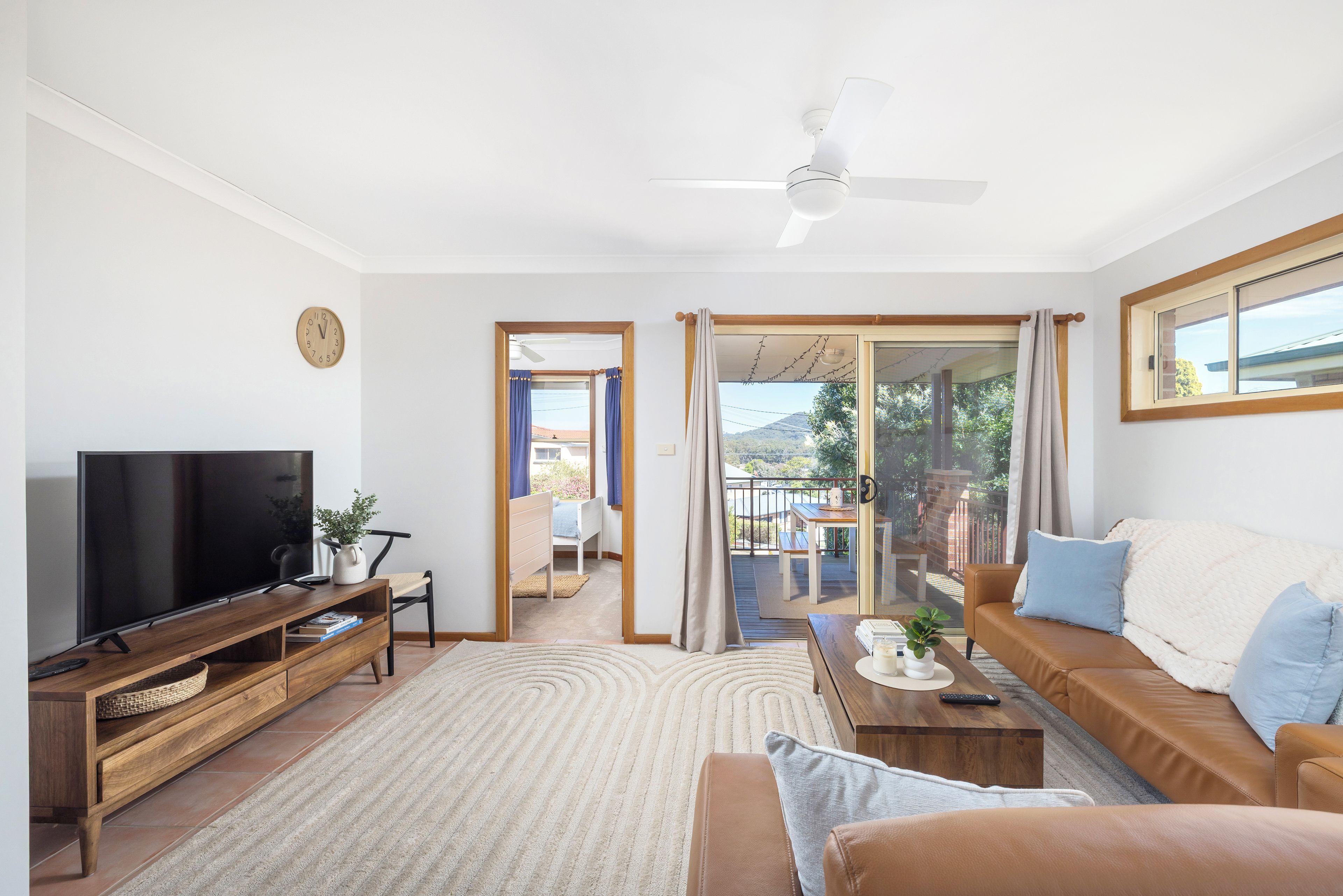 A modern living room with a flat-screen TV, wooden furniture, a sofa, and a view to an outdoor balcony.