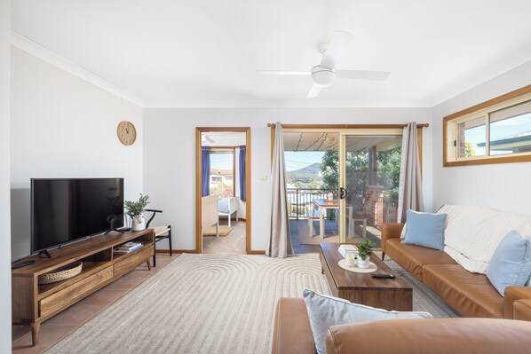 A modern living room with a flat-screen TV, wooden furniture, a sofa, and a view to an outdoor balcony.