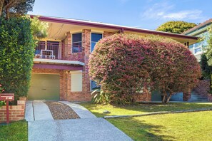A two-story house with a garage, a balcony, and a large flowering bush.