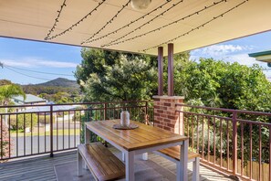 Une terrasse en bois avec une table et un banc, une cheminée en briques et une vue sur un paysage verdoyant, avec des arbres et une colline.