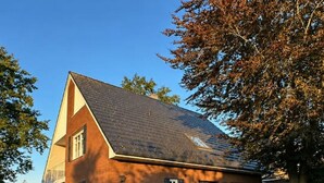 A two-story house with a sloped roof, a visible chimney, and a garden with hydrangea bushes. - Emsblick & Naturglück – Auszeit in Fresenburg (Fresenburg)