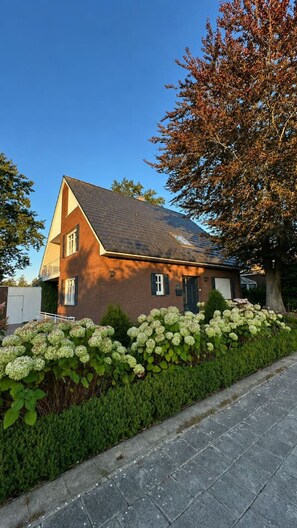 A two-story house with a sloped roof, a visible chimney, and a garden with hydrangea bushes. - Emsblick & Naturglück – Auszeit in Fresenburg (Fresenburg)