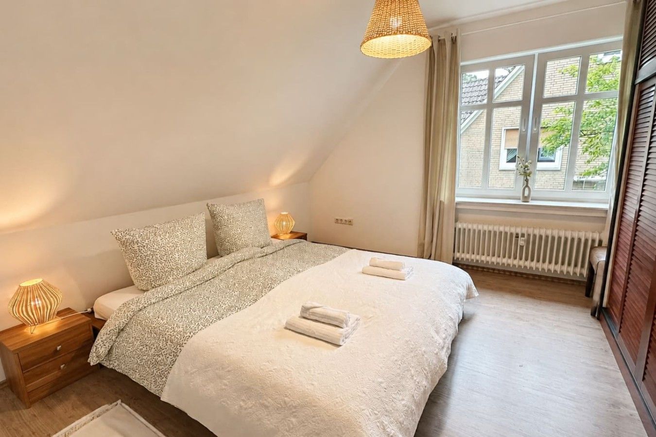 Ein Schlafzimmer mit einem Bett, Nachttischlampen, einem Fenster mit Vorhängen und einer Heizung.