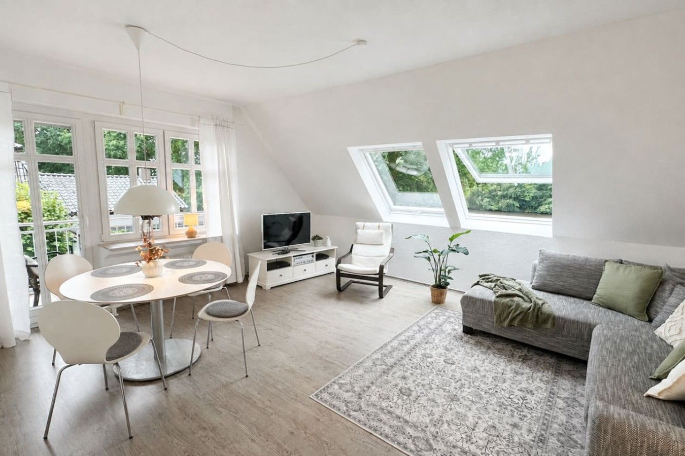 A modern living room with a dining area, a sofa, a TV, and a large window.