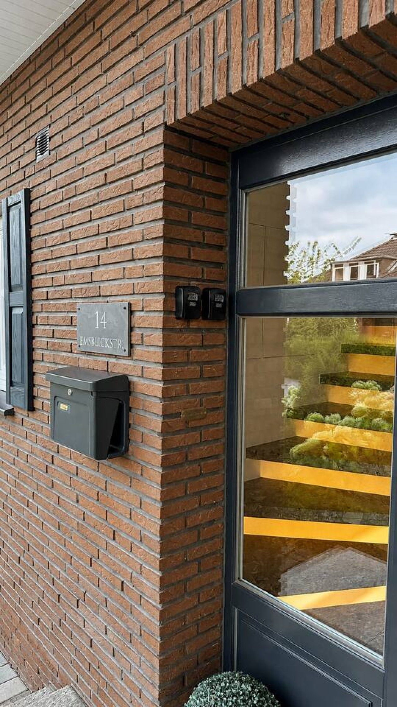 Ein Backsteinhaus mit großer Glastür, Briefkasten und einer Adresse.