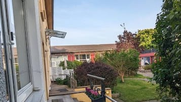 Un balcó amb una cadira i un taulell, un pont d'obra i vistes a una zona residencial amb cases i vegetació.