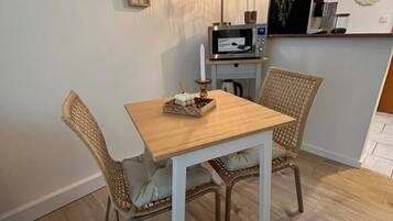 A dining area with a wooden table and wicker chairs, a wall-mounted lamp, and framed pictures.