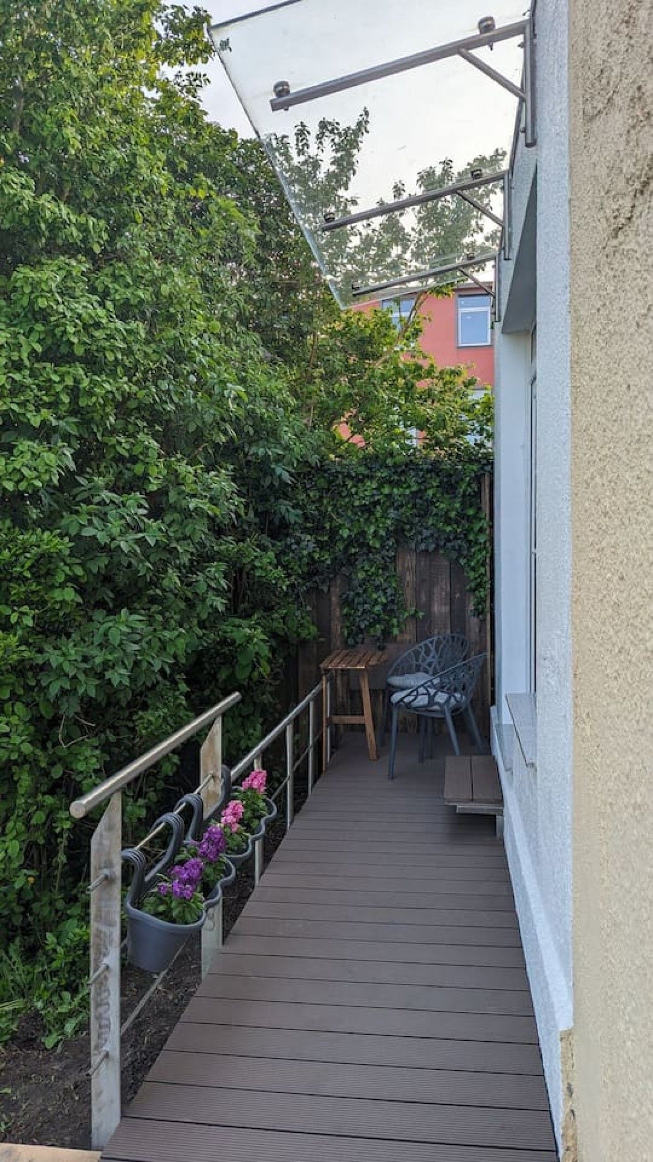 Eine Holzterrasse mit Metallgeländer, umgeben von dichter Vegetation und einem Holzzaun.