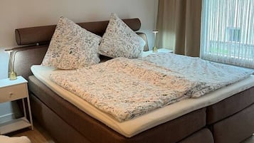 Un dormitori amb un llit, taules de nit, una làmpada i una finestra amb cortines.