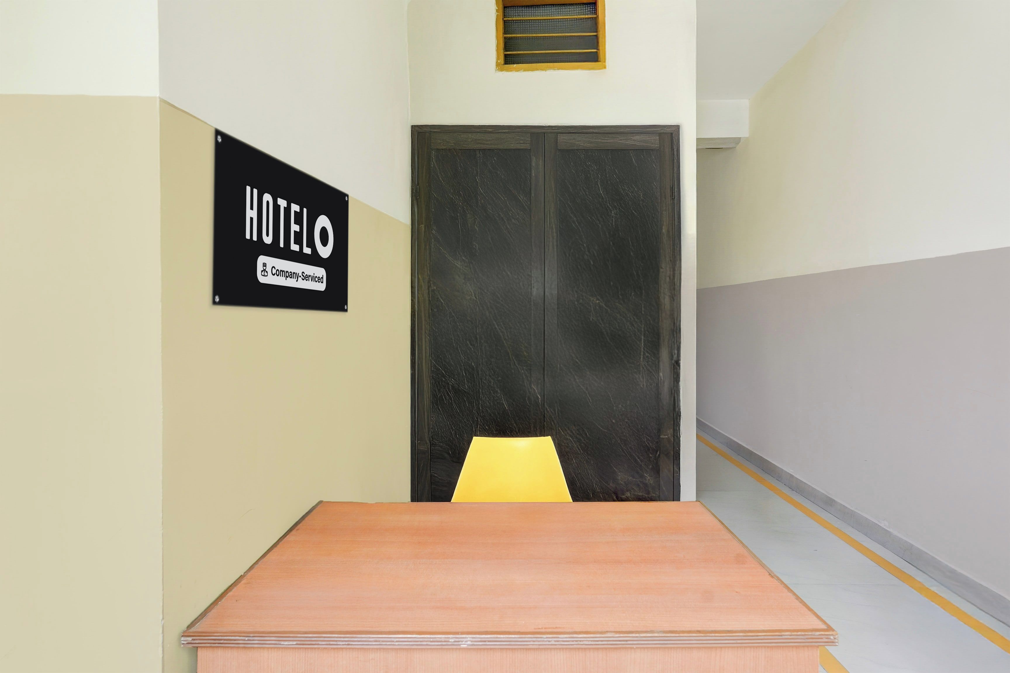 A hotel room with a wooden table, a yellow chair, and a sign indicating the room is company-serviced.