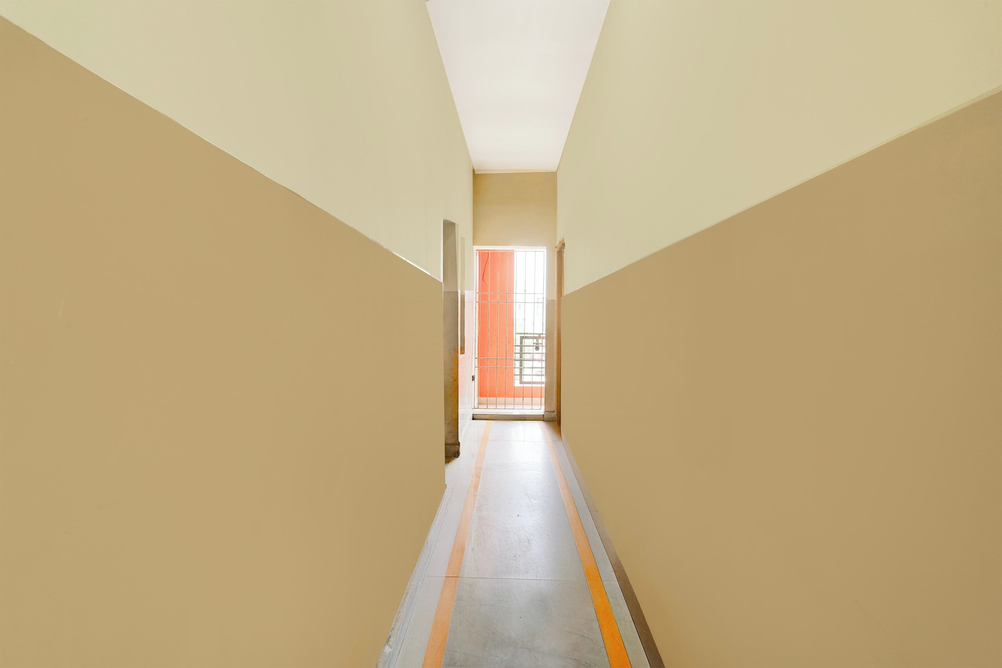 A corridor with beige walls and a tiled floor, leading to an open door with a window.