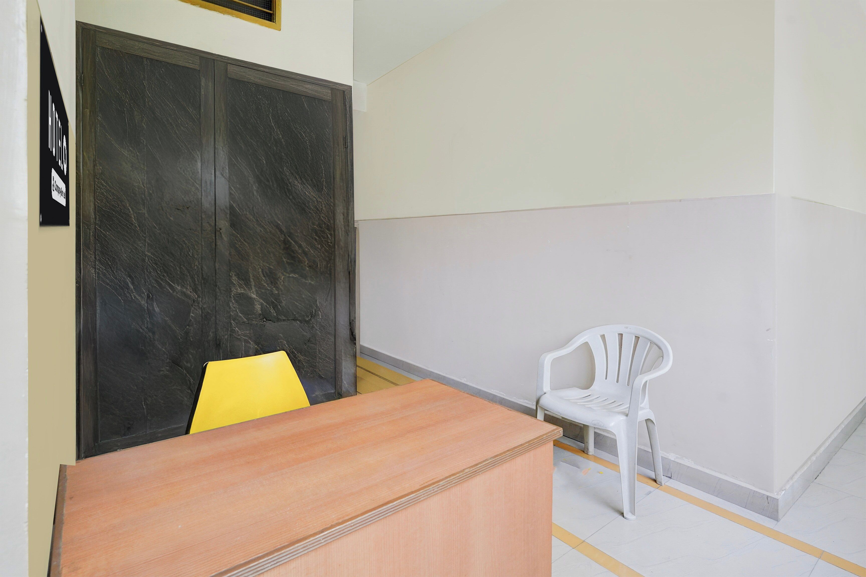 A room with a wooden desk, a yellow chair, a white plastic chair, and a black door.