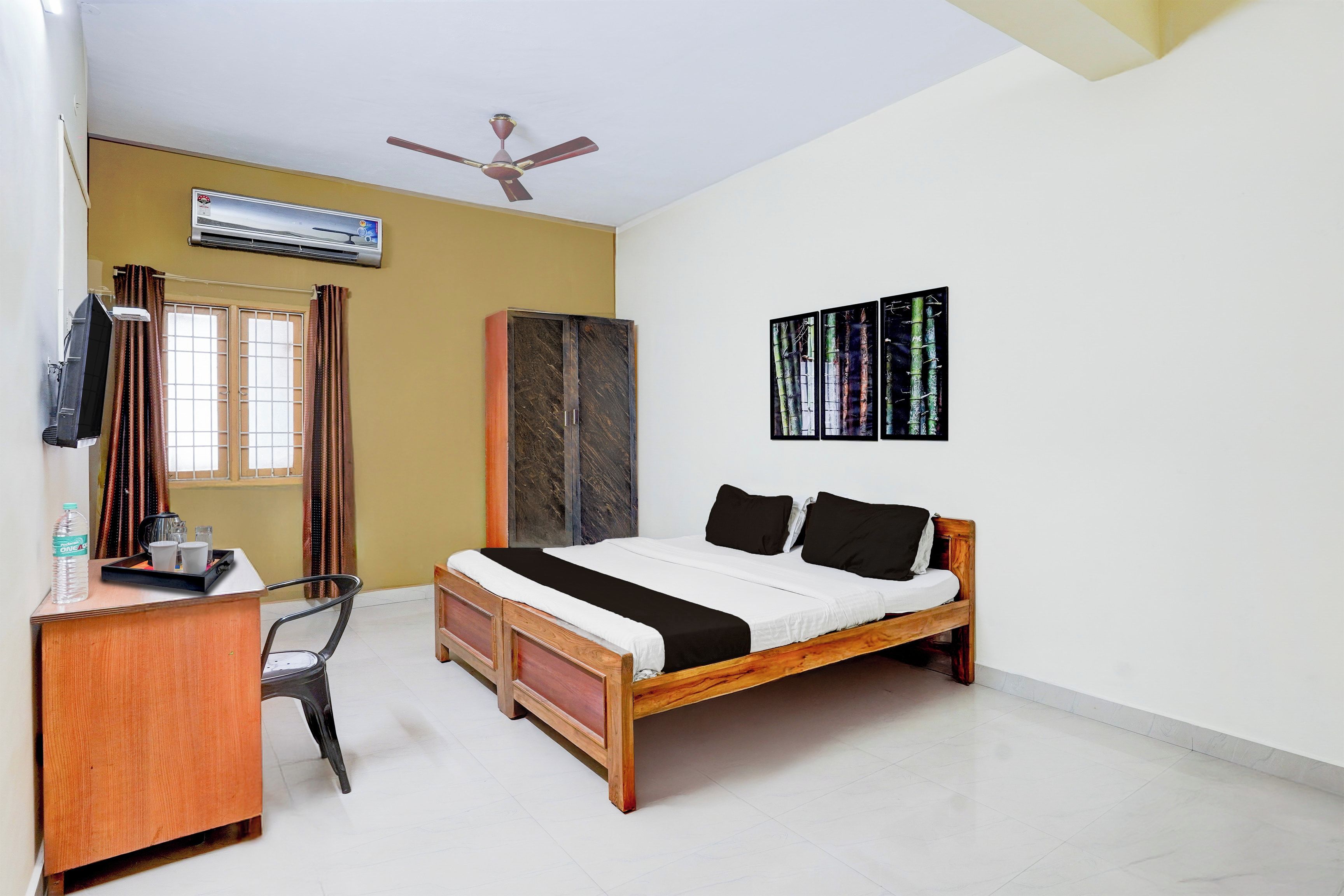 A bedroom with a bed, a desk, a chair, an air conditioner, a wardrobe, and a ceiling fan.