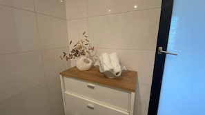 Une salle de bain avec un meuble-lavabo en bois, un porte-serviettes blanc et un vase contenant des fleurs séchées.