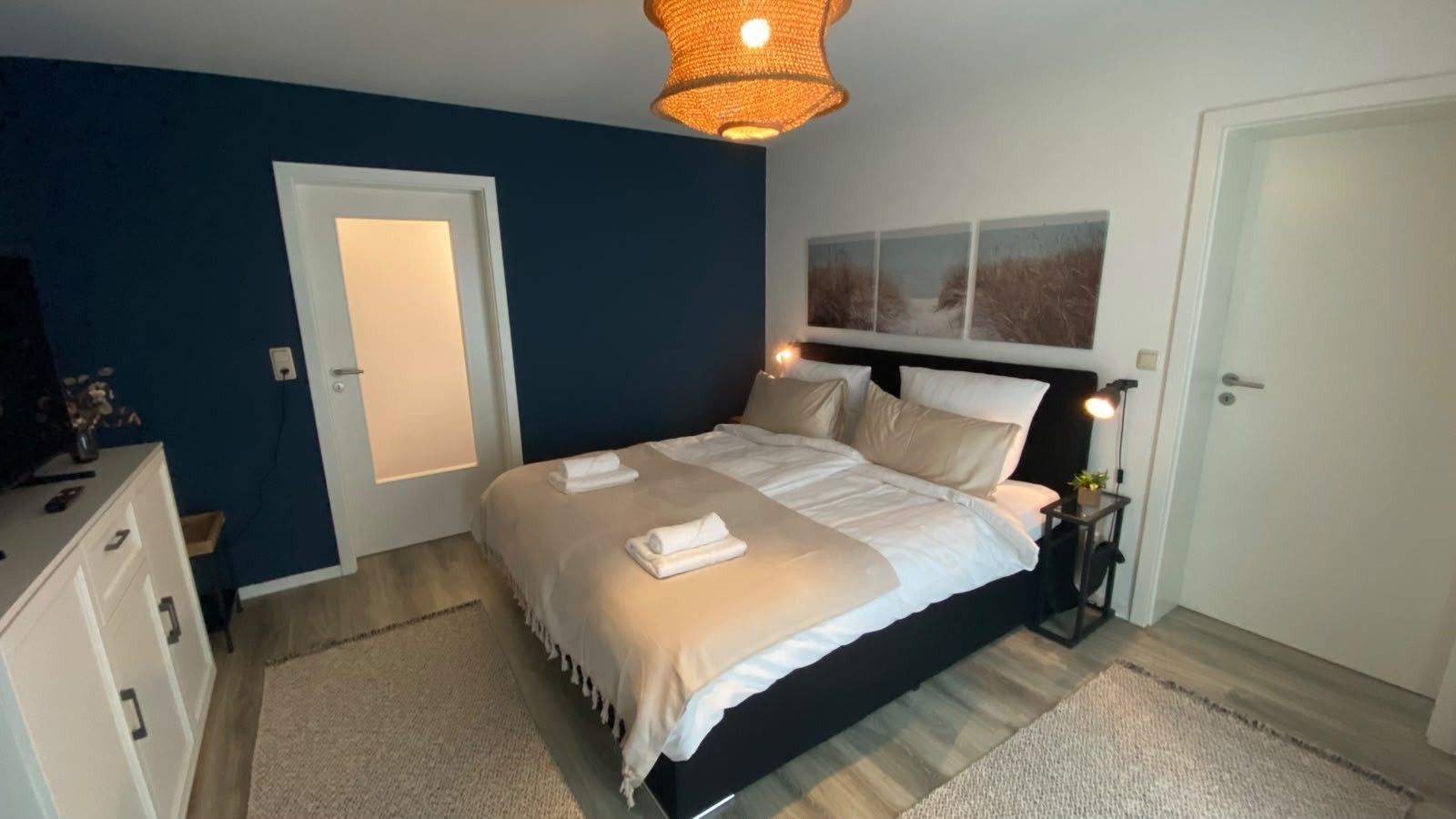 Ein Schlafzimmer mit einem Bett, Nachttischen, einer Tür und einem Wandbild.