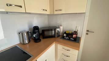 A kitchenette with a coffee maker, microwave, kettle, and a coffee bar with various items.