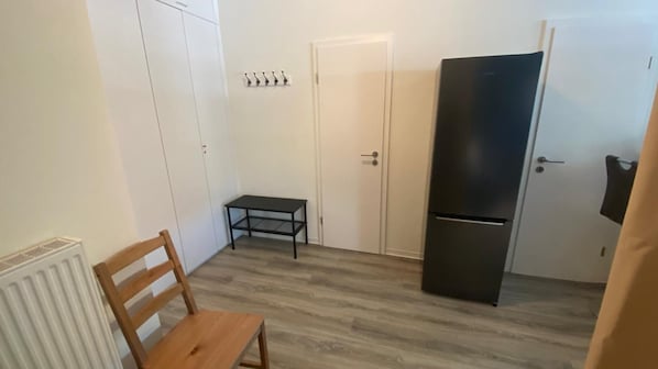 Une pièce de taille modeste, avec une chaise en bois, une petite table, un réfrigérateur noir et une porte blanche.