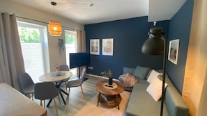 Uma sala de estar moderna com sofá, mesa de centro redonda, mesa de jantar com cadeiras, televisão e um abajur de chão grande.
