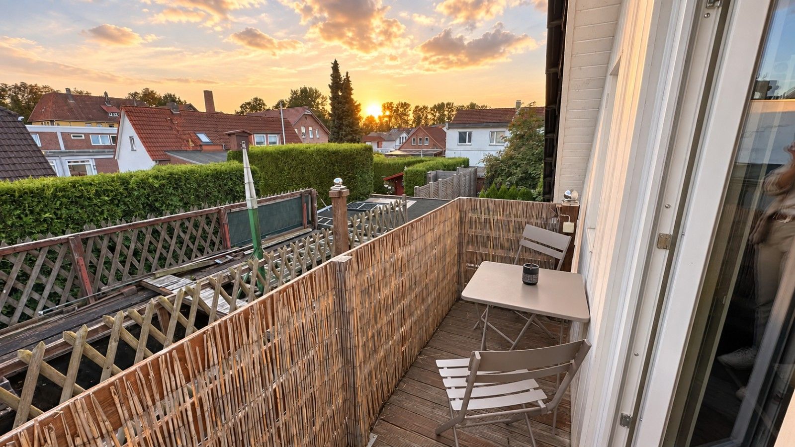 Un balcón con mesa y sillas, una cerca de madera y vista a casas al fondo.