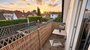 Un balcón con mesa y sillas, una cerca de madera y vista a casas al fondo.