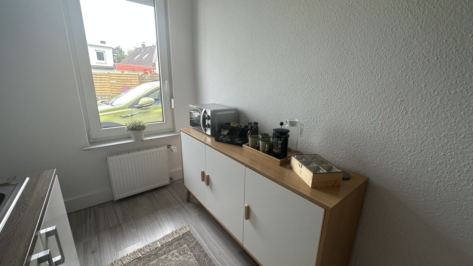 Una pequeña kitchenette con ventana, un radiador y una encimera con equipo para preparar café.