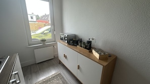 Una pequeña kitchenette con ventana, un radiador y una encimera con equipo para preparar café.