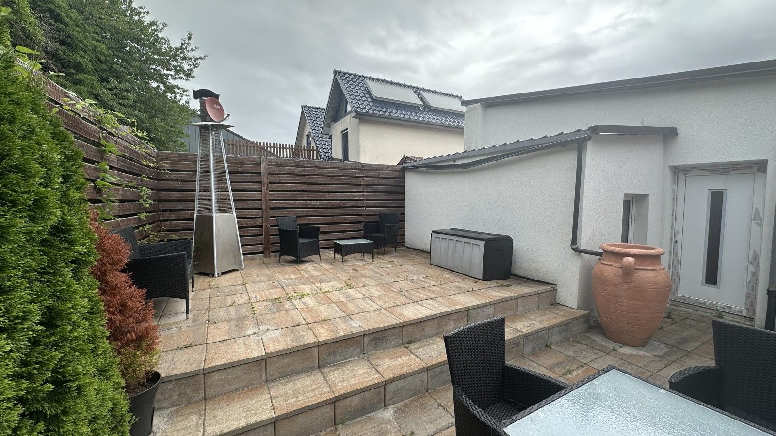 Eine Terrasse mit Grill, Sitzgelegenheiten im Freien und einem großen Terrakottatopf.