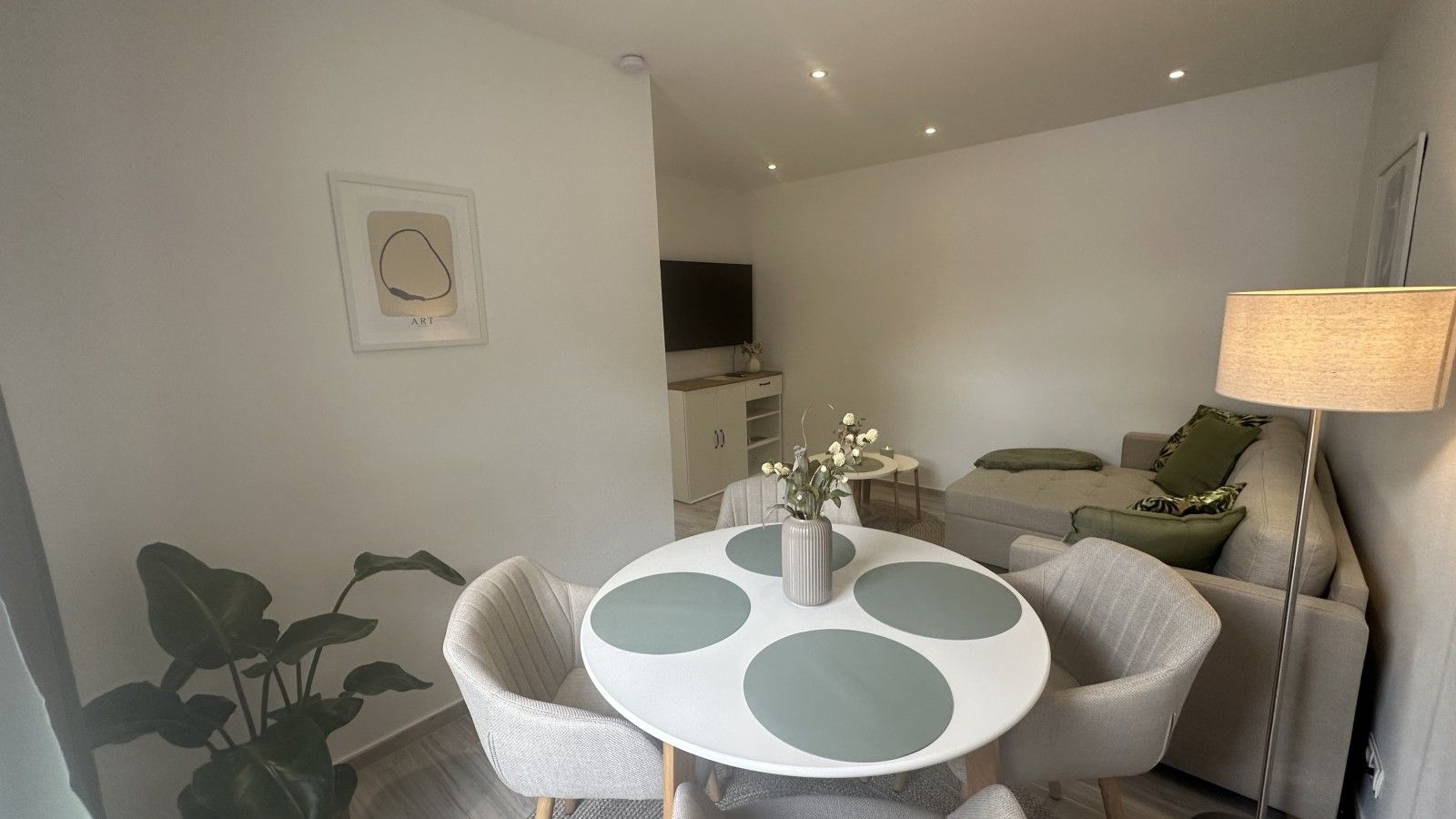 Una sala de estar moderna con una mesa redonda, sofás grises, una lámpara y una planta.