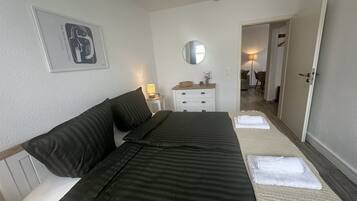 Habitación de hotel con cama, mesita de noche con lámpara, espejo y puerta que da a otra habitación.
