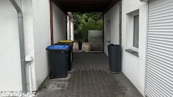 Ein überdachter Außenbereich mit gepflastertem Weg, Kiesfläche und zwei Mülleimern.