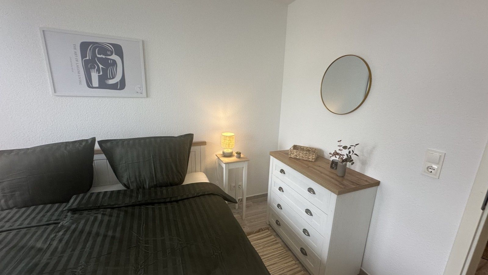 A bedroom with a bed, a bedside lamp, a dresser, and a framed picture on the wall.