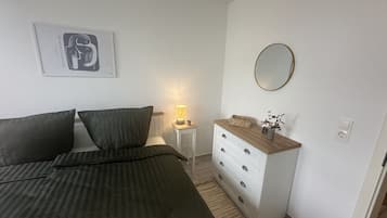 A bedroom with a bed, a bedside lamp, a dresser, and a framed picture on the wall.