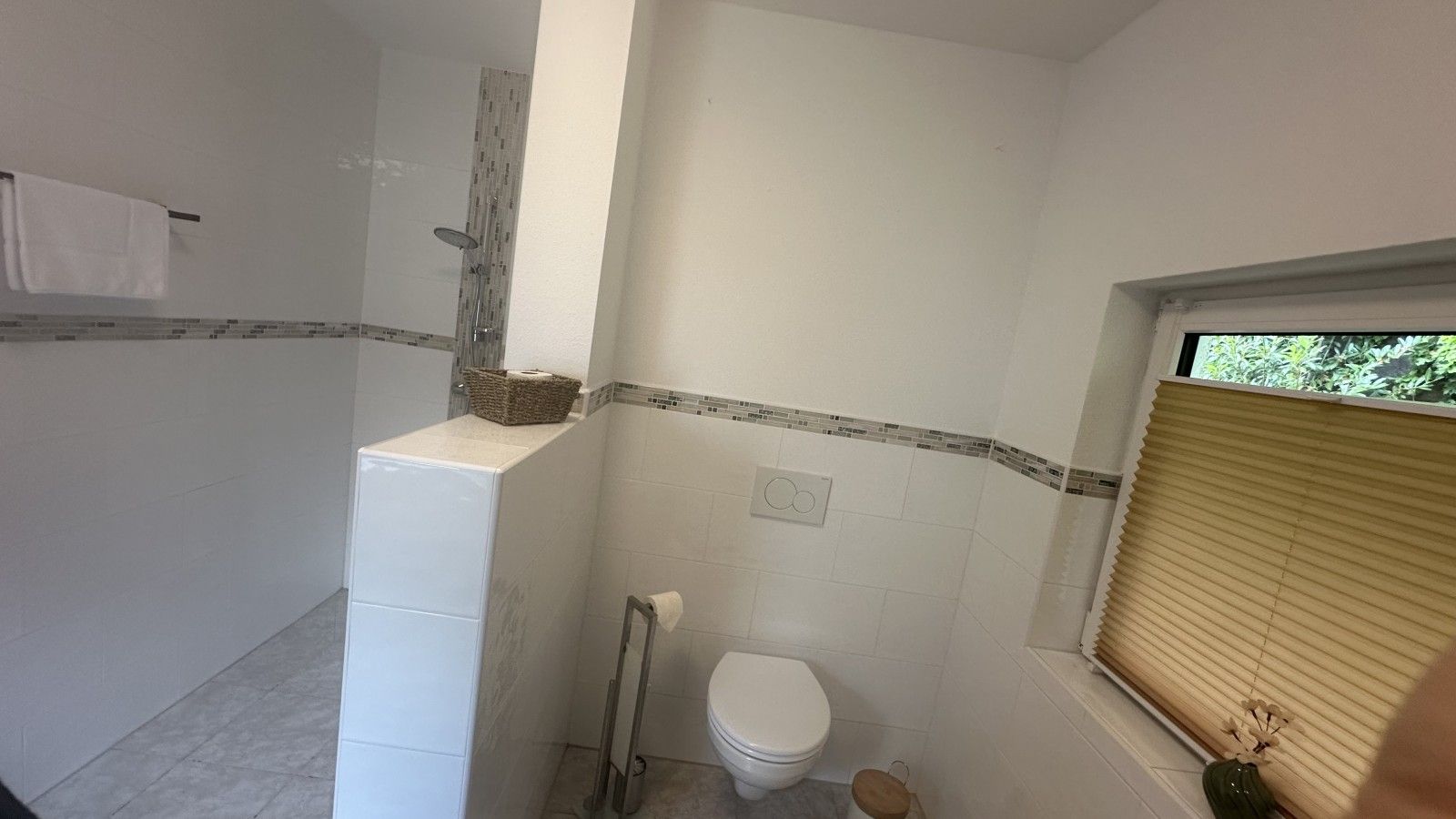 Ein Badezimmer mit Toilette, Dusche und einem Fenster mit Jalousien.