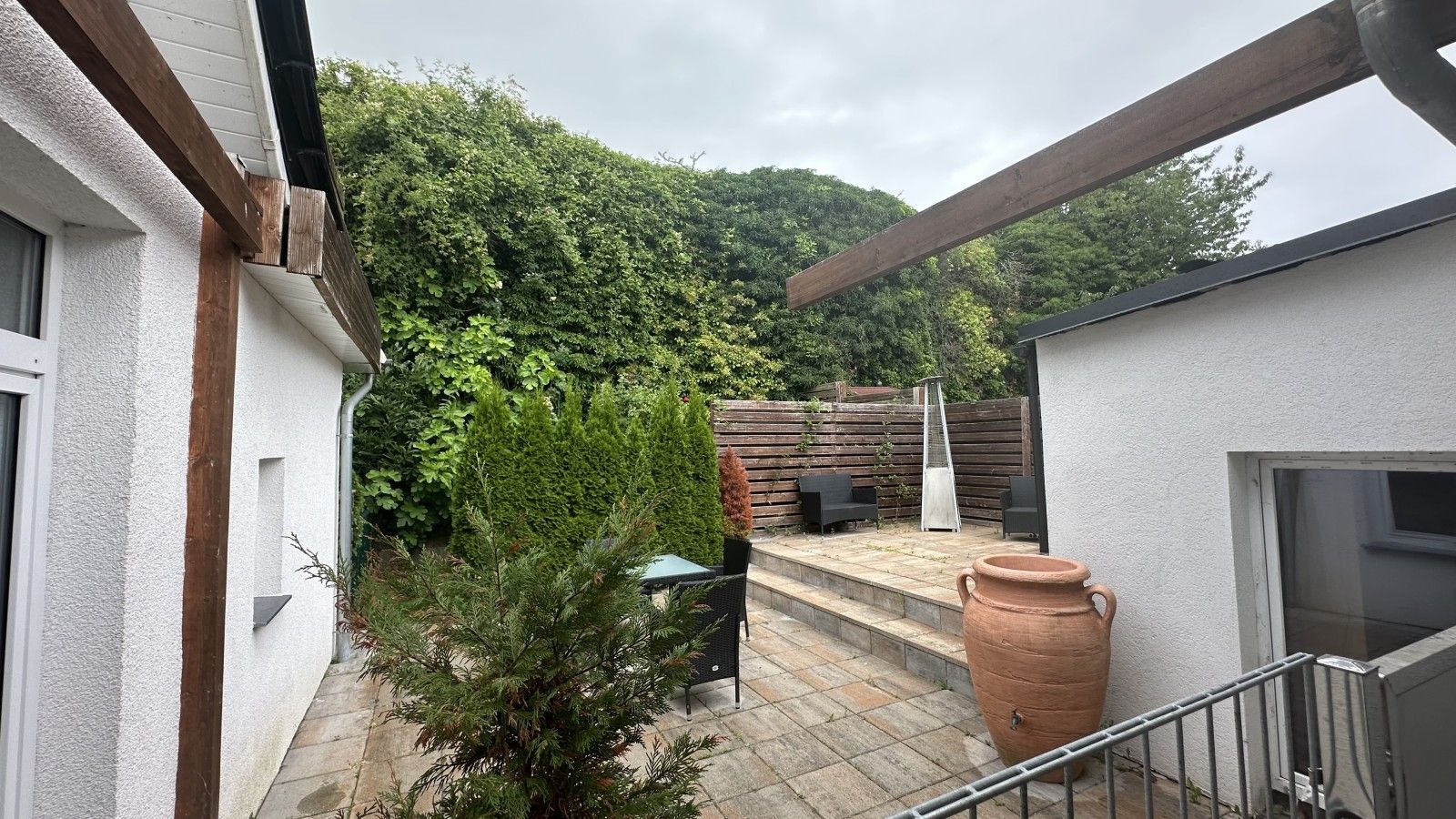 Un espacio de patio con cubierta de madera, una planta en maceta, mobiliario exterior y una maceta de terracota grande.