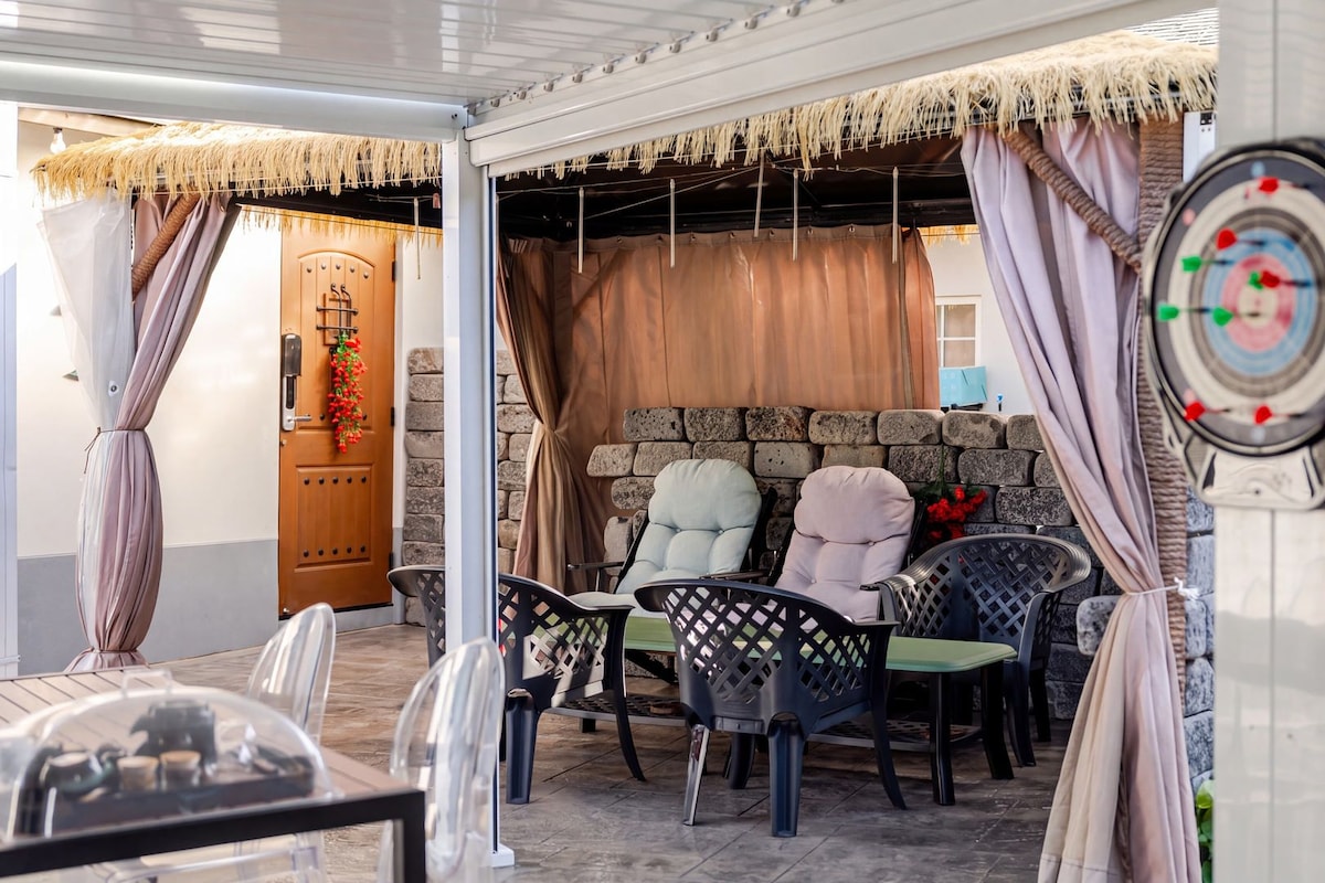 Un espace extérieur aménagé avec des chaises et une table, un mur en pierre et une porte ornée d’une guirlande décorative.