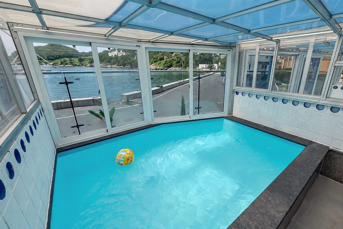 Une piscine intérieure, entourée de baies vitrées, offrant une vue sur l’eau et le paysage.