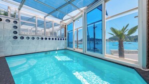 Une piscine dotée d’un toit en verre et de grandes fenêtres offrant une vue sur la mer.