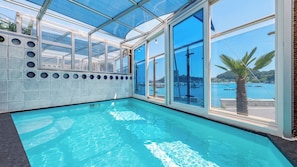 A swimming pool with a glass ceiling and large windows offering a view of the sea. - Namhae Tteul Pool Villa Pension (Namhae-gun)