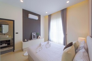 A hotel room with a bed, a bedside table, a mirror, a window with curtains, and an air conditioning unit. - 3BR Luxury Pool Villa, Hua Hin (TP3) (Hua Hin)