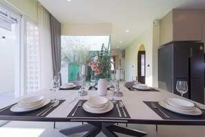 A dining area with a table set for four, a black refrigerator, and a view of a garden through a glass door. - 3BR Luxury Pool Villa, Hua Hin (TP3) (Hua Hin)