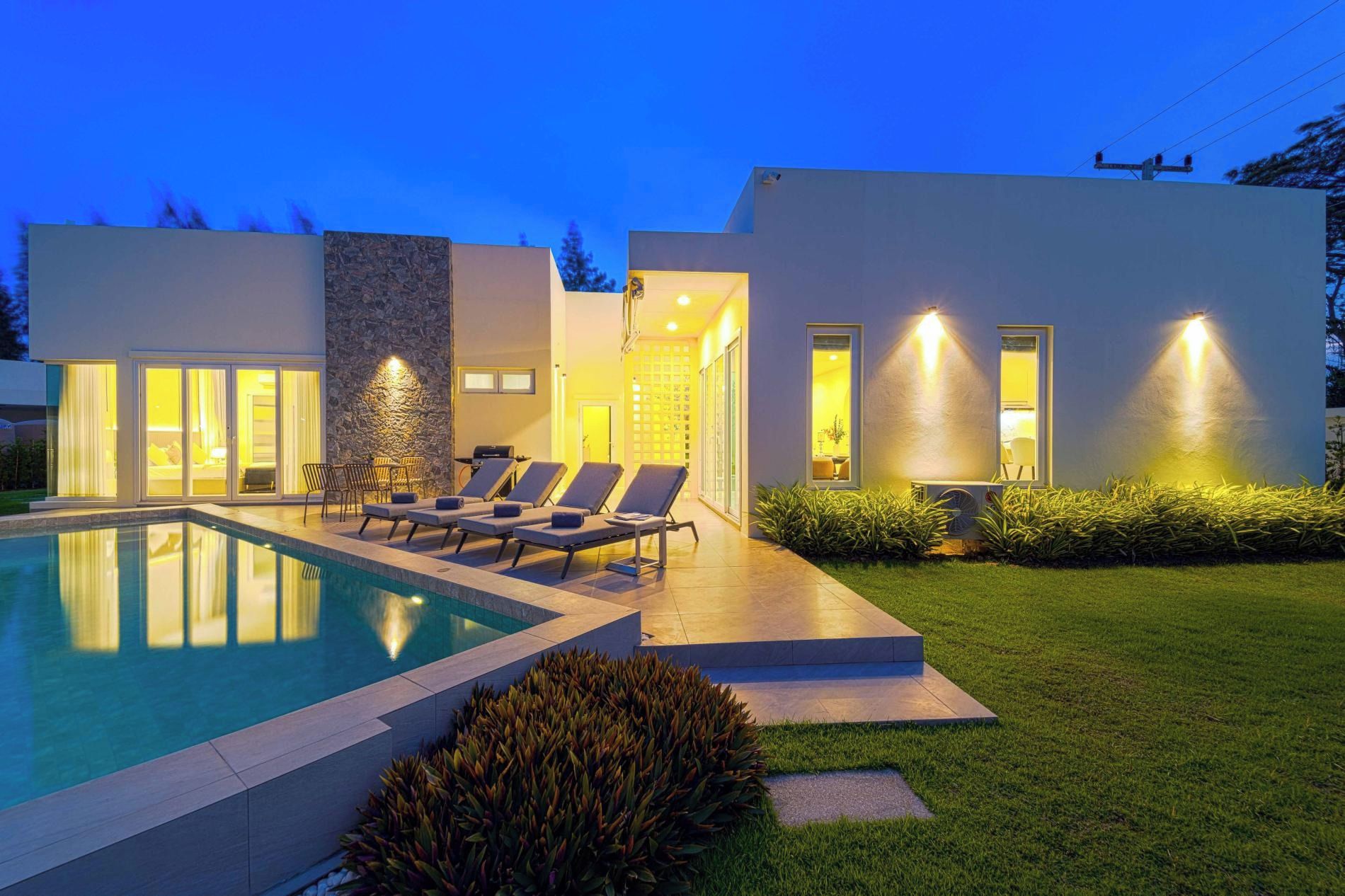 A modern house with a swimming pool, lounge chairs, and a well-lit exterior.