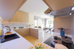 A modern kitchen with a marble backsplash, a central island, and a dining area with a table and chairs. - 3BR Luxury Pool Villa, Hua Hin (TP3) (Hua Hin)