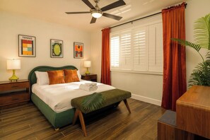Een hotelkamer met een bed, een plafondventilator, een raam met gordijnen en wanddecoratie met sportthema.