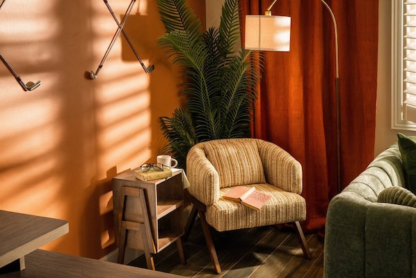 A cozy room with a wooden chair, a small table with a book and glasses, a lamp, and a large plant.