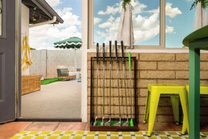 An indoor space with a window, a wall-mounted rack of golf clubs, a yellow stool, and a checkered floor mat.