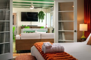 Ein Hotelzimmer mit Bett, Fernseher, Schreibtisch mit Stuhl, einer Pflanze und einem Fenster.