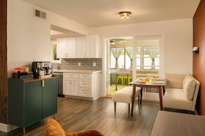 A compact kitchen with a coffee machine, a dining area with a table and chairs, and a view of the outside through a window.