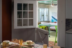 An open door leading to a dining area with a table and chairs, a window with curtains, and a ceiling fan.