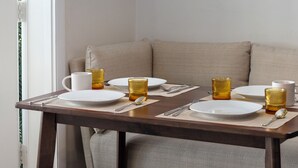 Een eettafel gedekt met borden, bestek en glazen, in een kamer met een bank en een raam.